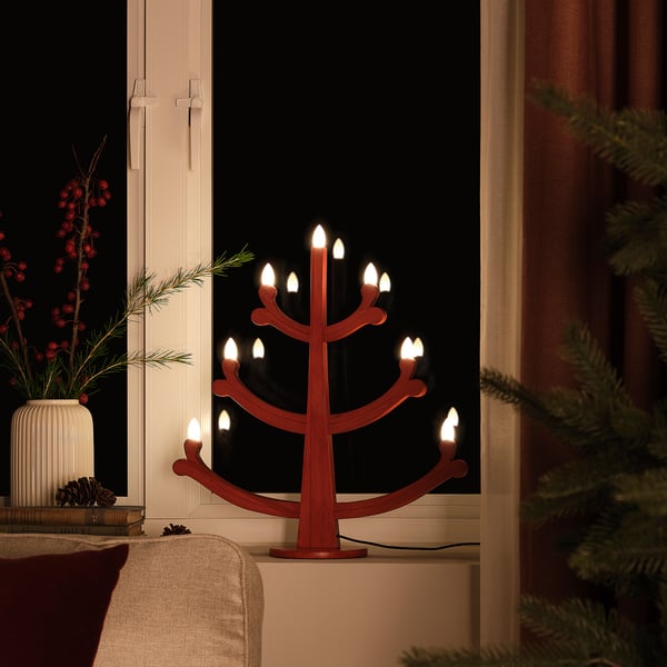 Candelabro vermello con lámpadas led na xanela, creando unha atmosfera cálida e acolledora.