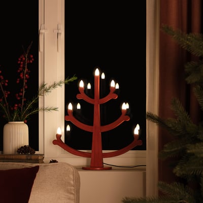 Candelabro vermello con lámpadas led na xanela, creando unha atmosfera cálida e acolledora.