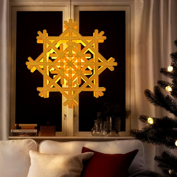 Sala de estar acolledora con lámpada de bambú, sofá e árbore de Nadal. Un brillo cálido xunto á fiestra.