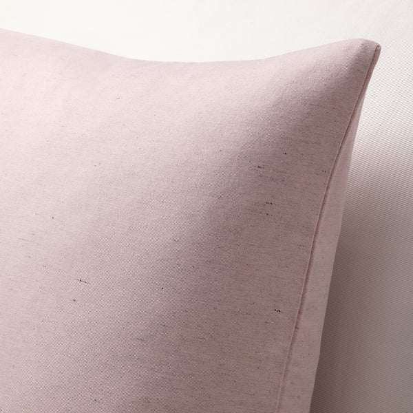 Primeiro plano de cuberta de coxín rosa claro suave e texturizada contra unha superficie correspondente. Detalle de costuras e tecidos sutil efecto slub visible.