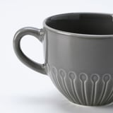 Cunca de cerámica gris escuro cun mango suave e patrojo floral texturizado preto da base. Acabado acristalado, deseñado cun aspecto moderno e limpo.