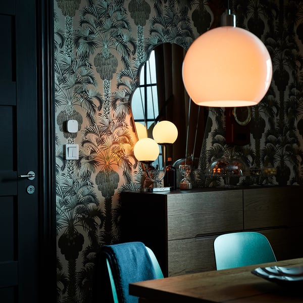 Zona de comedor moderna con cadeiras verde azul, sideboard negro, luminaria globo branco e fondo de pantalla botánico.