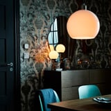 Zona de comedor moderna con cadeiras verde azul, sideboard negro, luminaria globo branco e fondo de pantalla botánico.