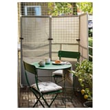 Pequeno balcón acolledor con mesa e cadeiras de metal verde, asentos acolchados, limón e pantalla de privacidade en rede.