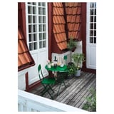 Pequeno balcón con mesa e cadeiras verdes SUNDSÖ, edificio branco, plantas en pota, teito de tella vermella.