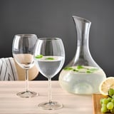 Dous vasos de viño e unha carafa de auga con franxas de limón sobre unha mesa.