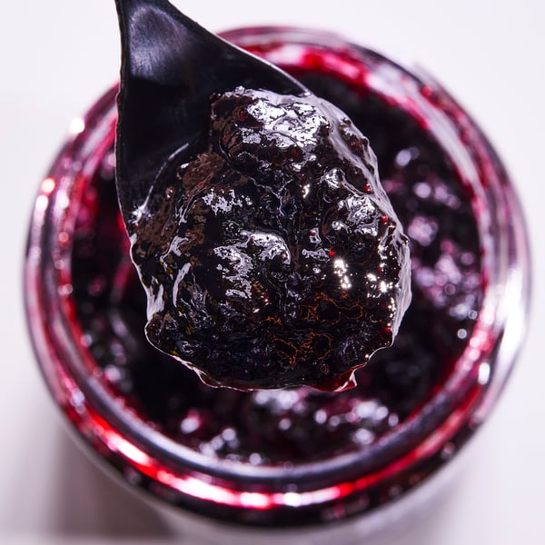 Un frasco de marmelada de blueberry escuro orgánico cunha culler suxeita enriba.