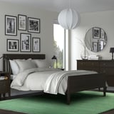 Dormitorio con mobles de madeira escura, unha gran cama branca, fotos enmarcadas, espello redondo, luz colgante e unha alfombra verde. A alfombra ten un tamaño: grande.