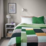 Dormitorio acolledor con cuberta de cama TALLSVÄRMARE, lámpadas e libros.