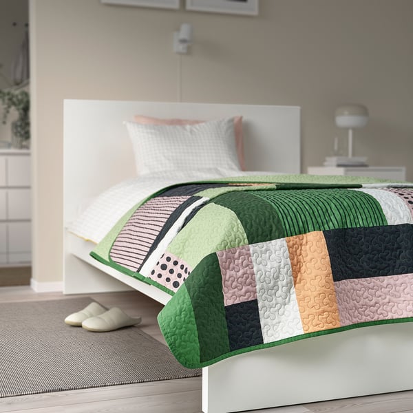 Gran cuberta de cama quilted multicolor cobre a cama, cabeceira branca, almofadas pastel.