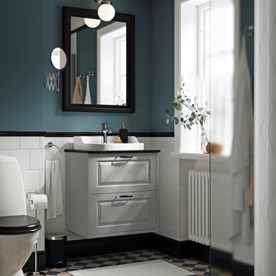 Un baño moderno cunha vanidade gris TÄNNFORSEN, con dous caixóns, un lavabo cerámico e un deseño gris e branco cohesionado.