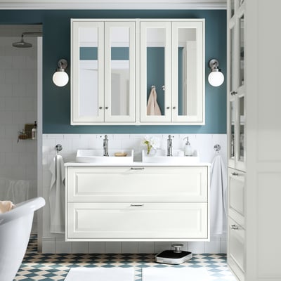 Baño branco moderno con gran unidade de vanidade, lavabo e armario de espello. O chan ten baldosas azul-grises. Toallas montadas, luminarias e accesorios.