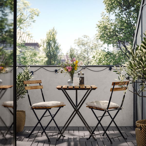 Pequenos asentos ao aire libre con mesa e dúas cadeiras, negro e madeira. Decorado con vasos de flores e luces de corda.