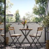 Pequenos asentos ao aire libre con mesa e dúas cadeiras, negro e madeira. Decorado con vasos de flores e luces de corda.
