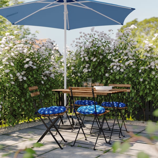 Pequeno conxunto de comedor ao aire libre con coxíns con patróns azuis e un paraugas correspondente, perfecto para xardíns de balcóns.