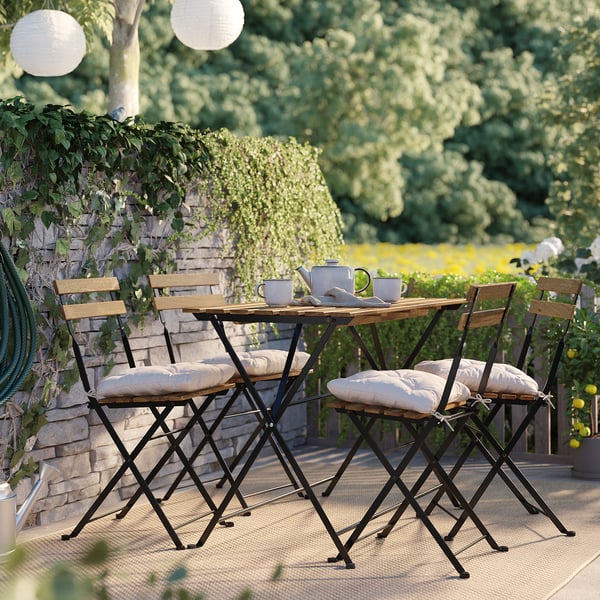Pequeno patio con mesa de madeira, 4 cadeiras, coxíns. Rodeada de verde, acolledores asentos ao aire libre.