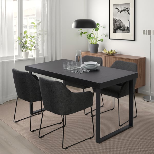 Comedor moderno con mesa negra TARSELE, catro cadeiras, lámpadas, planta. Deseño minimalista baixo a fiestra, preto do taboleiro de madeira.