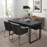 Comedor moderno con mesa negra TARSELE, catro cadeiras, lámpadas, planta. Deseño minimalista baixo a fiestra, preto do taboleiro de madeira.