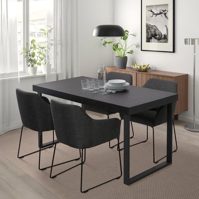 Comedor moderno con mesa negra TARSELE, catro cadeiras, lámpadas, planta. Deseño minimalista baixo a fiestra, preto do taboleiro de madeira.