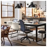 Zona de comedor moderna con revestimento negro TARSELE e mesa extensible metálica, cadeiras brancas, asento azul, lámpadas colgantes negras e cociña ao fondo.