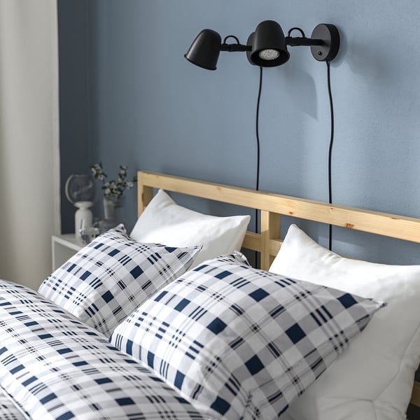 Unha cama acolledora e moderna cunha cabeceira de madeira, pivet de plaid e lámpadas de noite montadas na parede.