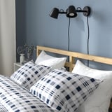 Unha cama acolledora e moderna cunha cabeceira de madeira, pivet de plaid e lámpadas de noite montadas na parede.