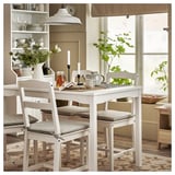 Conxunto de comedor branco con cadeiras acolchadas, inclúe mesa, teteira e velas. Estilo de granxa moderno con estantes abertos e alfombra.