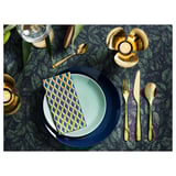 Mesa con cubertas de latón TILLAGD: coitelo, garfo, culler en pratos azuis con servilletas de ouro sobre mesa escura con patróns.