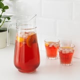 Xerra e vasos cheos de bebida xeada vermella, guarnición con franxas de laranxa. Un mango para un agarre fácil e un boca para verter.