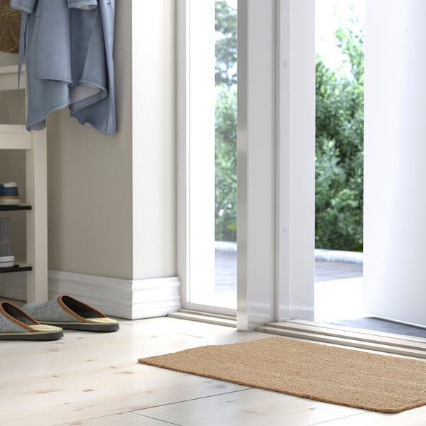 Entrada brillante con alfombra beige TIOKRONA, chaqueta azul, deseño limpo.