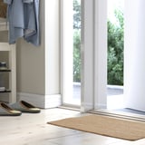 Entrada brillante con alfombra beige TIOKRONA, chaqueta azul, deseño limpo.