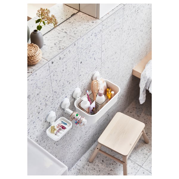 Organizador de baño de plástico branco con cepillos de dentes, xoias e taburete de madeira.