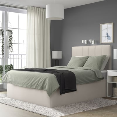 Dormitorio moderno con cama gris TJÅLLE, grande pola xanela, cabeceira de tecido claro, roupa de cama gris correspondente. Paredes grises, grandes cortinas, plantas colgantes.
