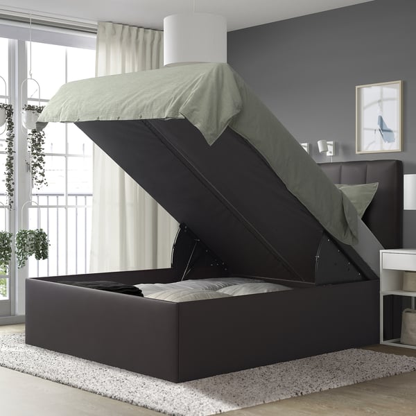 Dormitorio moderno con cama TJÅLLE, gris, grande, almacenamento, cabeceira de peluche, alfombra branca, plantas colgantes, paredes brancas, cortinas grises e arte.