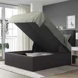 Dormitorio moderno con cama TJÅLLE, gris, grande, almacenamento, cabeceira de peluche, alfombra branca, plantas colgantes, paredes brancas, cortinas grises e arte.