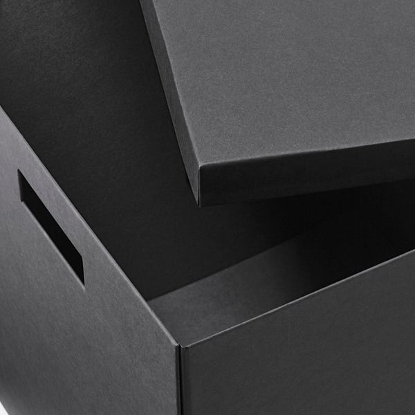 Caixas de cartón negro, apiladas ben apiladas. Caixa superior lixeiramente aberta, mostrando unha construción robusta. Material reciclado e de alta calidade.