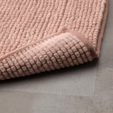 Unha alfombra de baño rosa claro con texturas elevadas para suavidade e secado rápido. Unha superficie de malla debaixo para o agarre é visible.