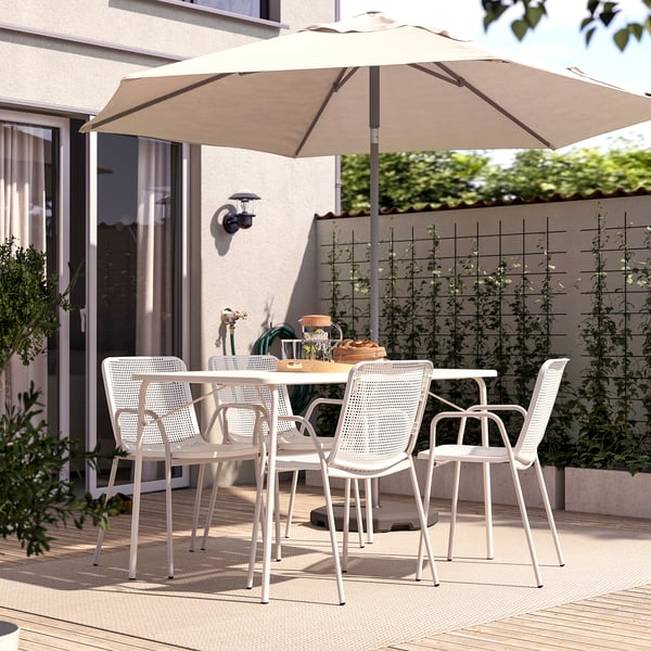 Patio exterior moderno con mesa e cadeiras brancas TORPARÖ, paraugas beige, colocado sobre cuberta de madeira, rodeado de verde.