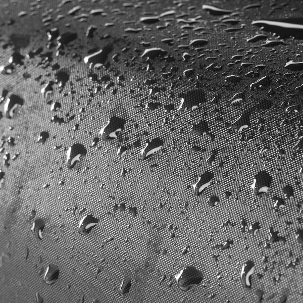 As gotas de auga brillan na superficie impermeable. Esta cuberta protectora mantén os mobles de exterior secos, organizados e duradeiros.