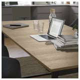 Unha moderna mesa de comedor transformable TRÄKUMLA nunha cor de madeira clara cun portátil, tableta e libros na parte superior.