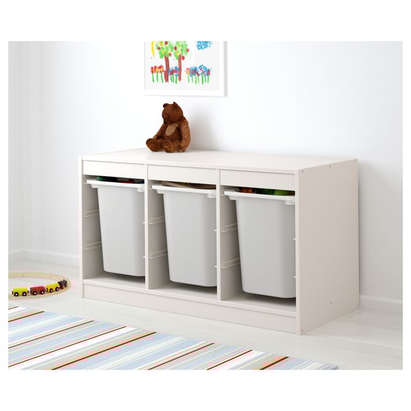 Unidade de almacenamento TROFAST branco con tres colectores grises extraíbles. Un oso de peluche está sentado enriba, ilustrando o fácil acceso para os nenos. Ideal para organizar xoguetes.