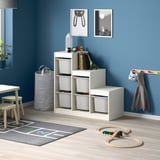 Sala de xogos infantís con almacenamento branco TROFAST, contedores grises, xoguetes de madeira e decoración en branco negro contra a parede azul.