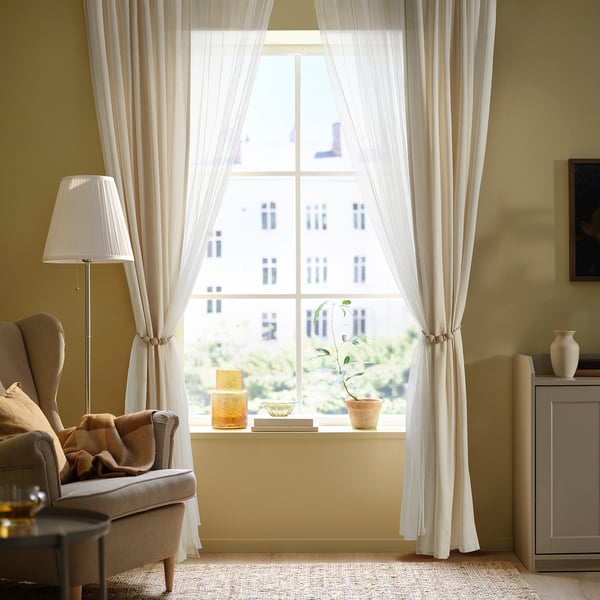 Sala de estar acolledora con suxeitos TRUBBRYUM , cadeira, lámpada e decoración de mesa. As cortinas esténdense do chan ao teito.