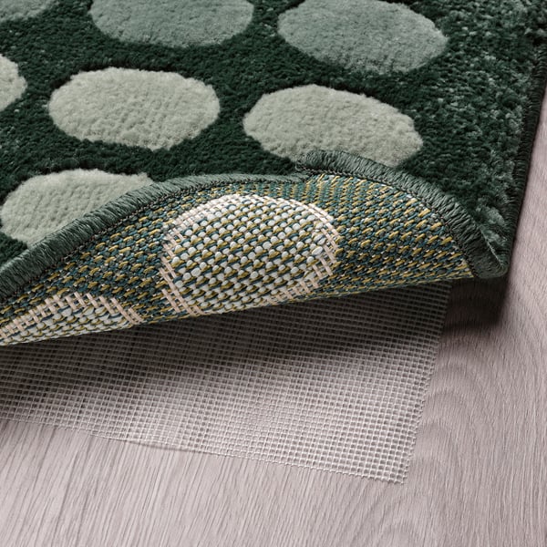 Alfombra verde con puntos brancos e malla antideslizante abaixo.