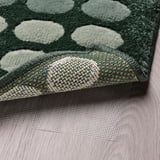Alfombra verde con puntos brancos e malla antideslizante abaixo.