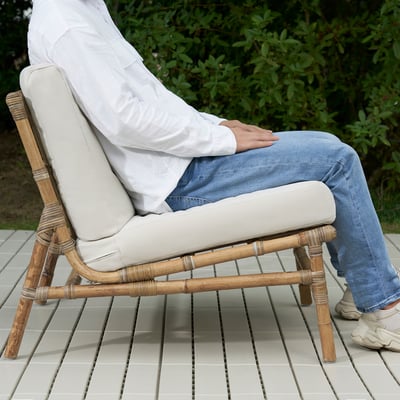 Persoa sentada na cadeira de ratán TVARÖ no patio, relaxada coas pernas cruzadas.