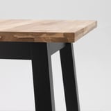 Primeiro plano dunha robusta mesa de madeira de acacia con patas de metal negro, acabada con laca acrílica clara.