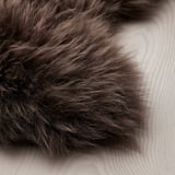 Primeiro plano de suave e luxosa alfombra de pel de ovella marrón sobre chan de madeira clara, mostrando a súa textura fluffy e beleza natural.