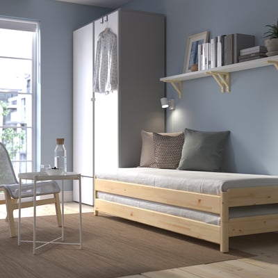 Dormitorio azul con cama UTÅKER, almofadas grises, estantes, mesa de vidro. Deseño eficiente no espazo.