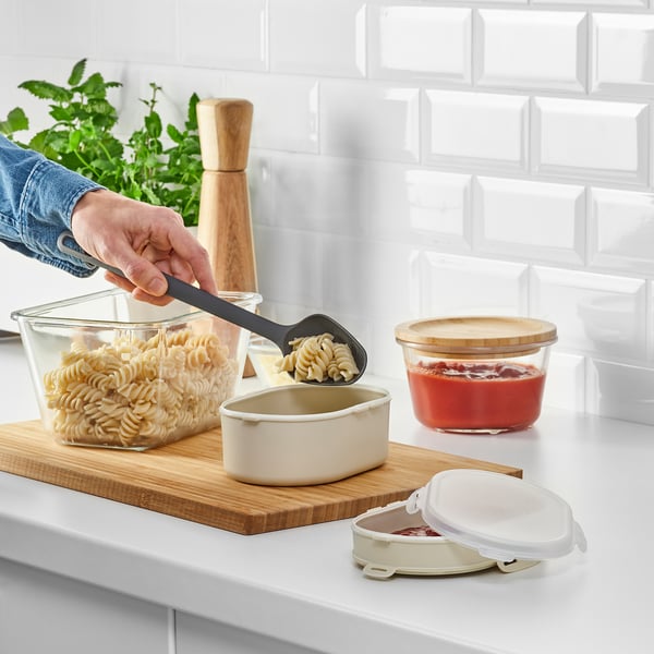 Persoa que recolle fideos nunha caixa de xantar apilable nunha táboa de madeira. A caixa de xantar ten compartimentos separados para comida seca.